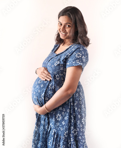 A pregnant indian lady with blue dress and hands on belly.