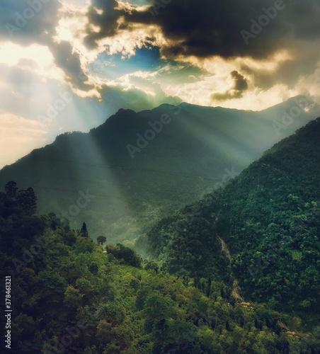 Sunrays hitting a green mountain vegetation from the clouds. © Arindam