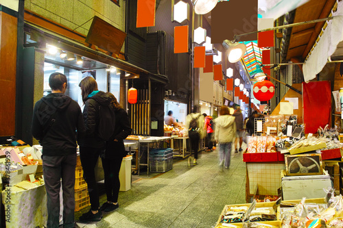 京都市の中心地にある錦市場内の店舗の景観。錦市場は、真ん中の小道の両側に食材の商店が並んだ３９０ｍの商店街。近年は外国人観光客を中心に賑わっている。