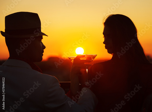 Romantic couple enjoying a glass of wine and beautiful sunset view. Couple drinking glass of cocktail together. Happy life moments. Cheers at sunset.