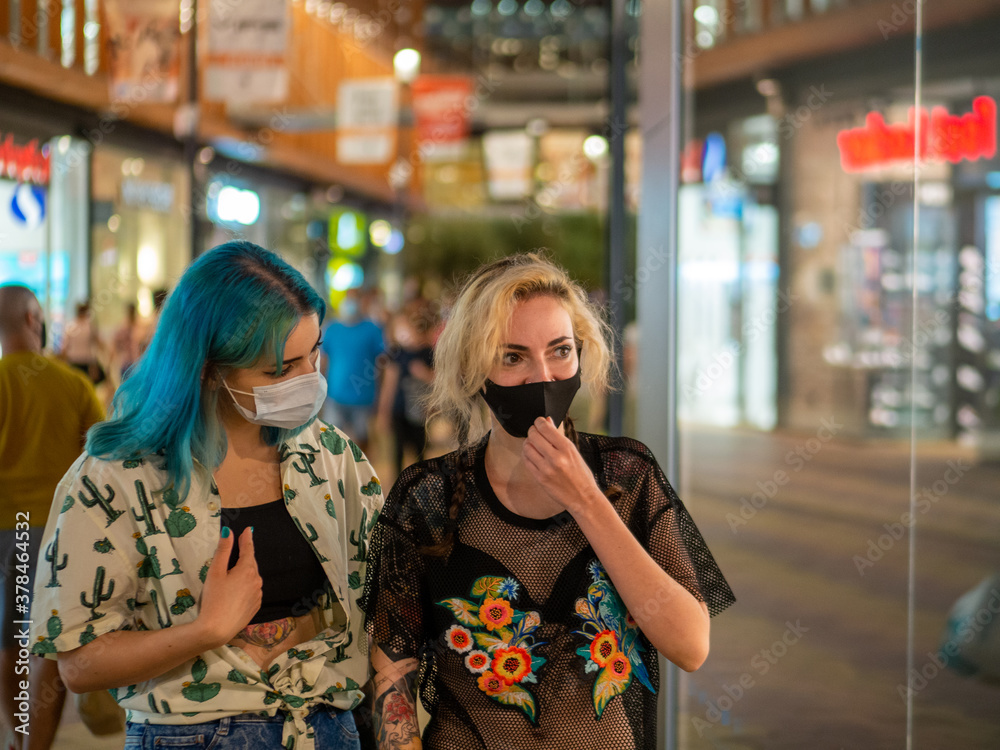 Mujeres jóvenes con mascarilla hablando respetando las medidas de seguridad y distanciamiento social de la pandemia del coronavirus