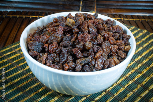 Raisins in a white bowl on a brown wooden mat.