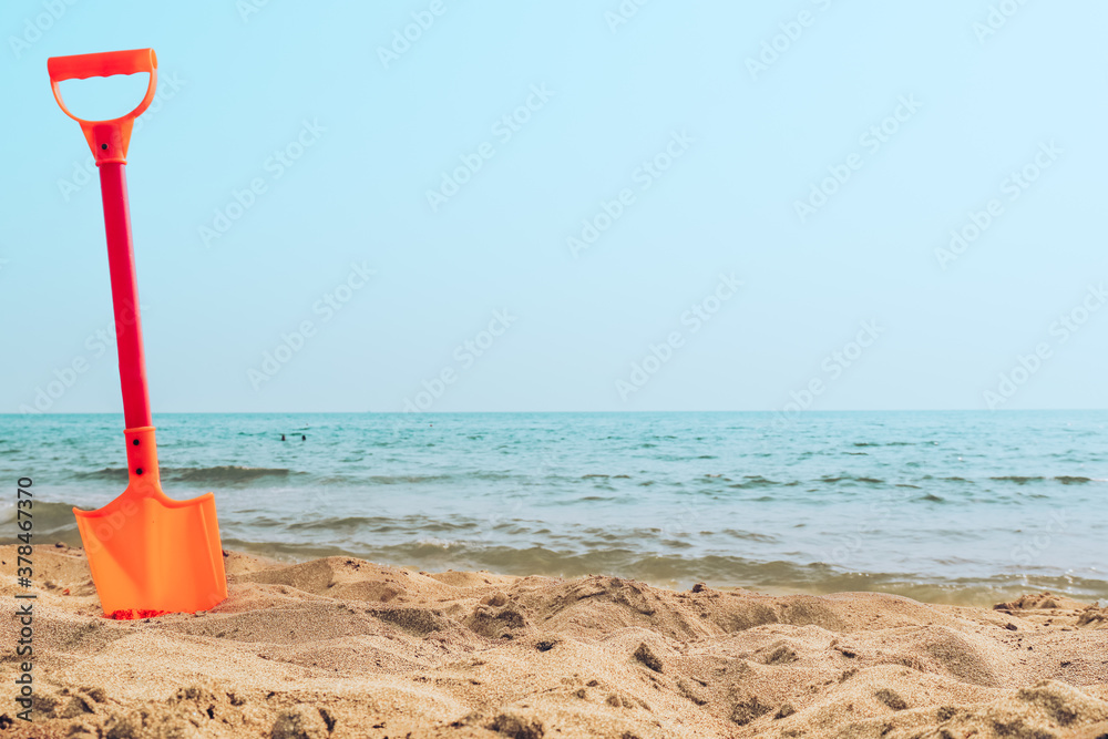 Kid's toy orange shovel stuck in a sand at the beach sea shore