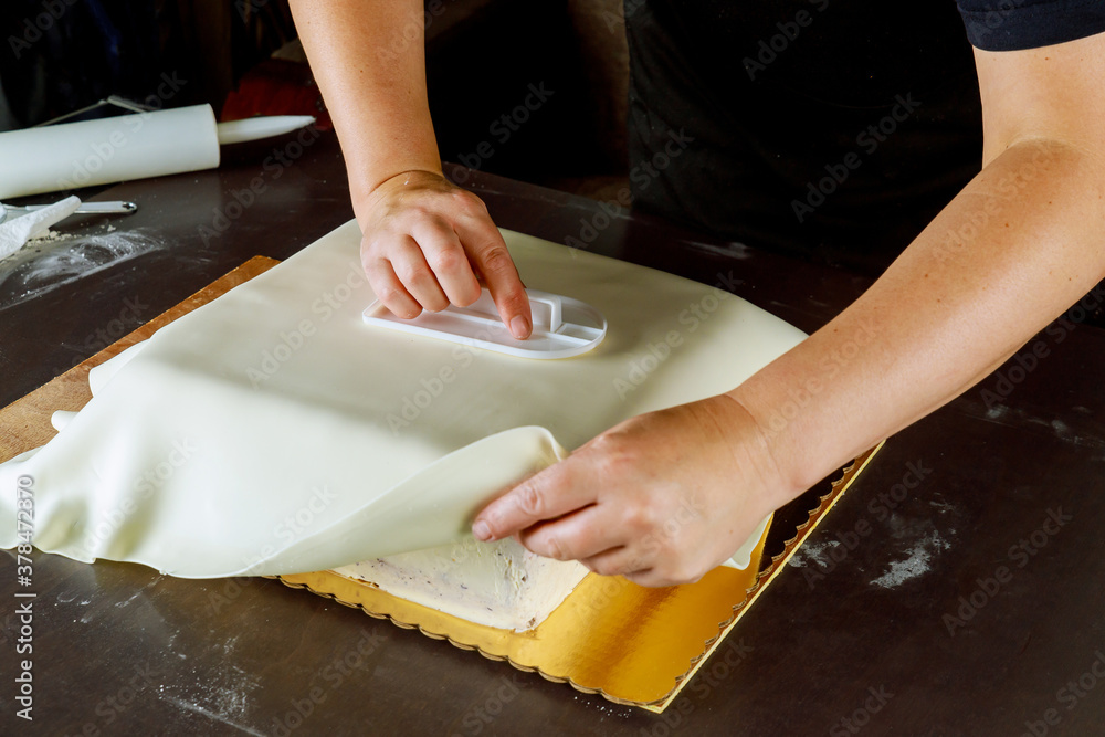 Baker covering square cake with white fondant.
