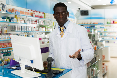 Experienced African American male pharmacist working on computer in modern pharmacy
