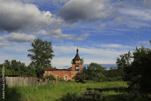 Ruined orthodox church in a Russian village on a sunny summer day and surrounded by flowers and trees