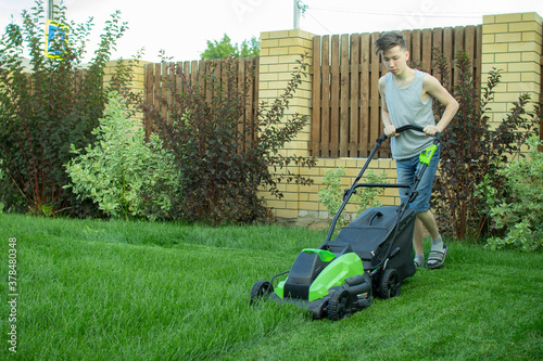 Obraz na plátně A teenager mows the lawn with a lawn mower.