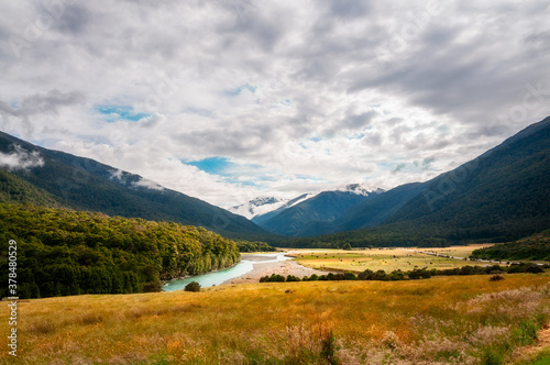 A patch of sunlight at Cameron Flat s picturesque landscape in Mount Aspiring National Park along Makarora River  with snow-capped mountain peaks engulfed in clouds in New Zealand  South Island.