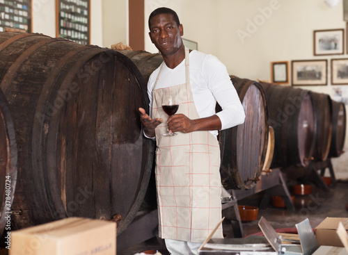 Confident male winemaker inviting to a wine shop, offering glass of a red wine for tasting photo