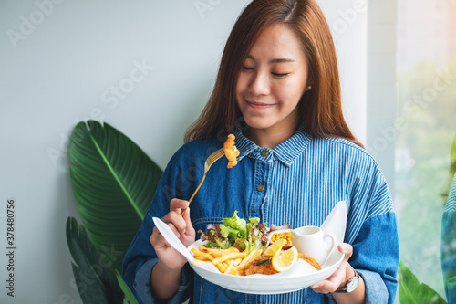 Photography Closeup image of a beautiful asian woman eating fish and chips on table in the r