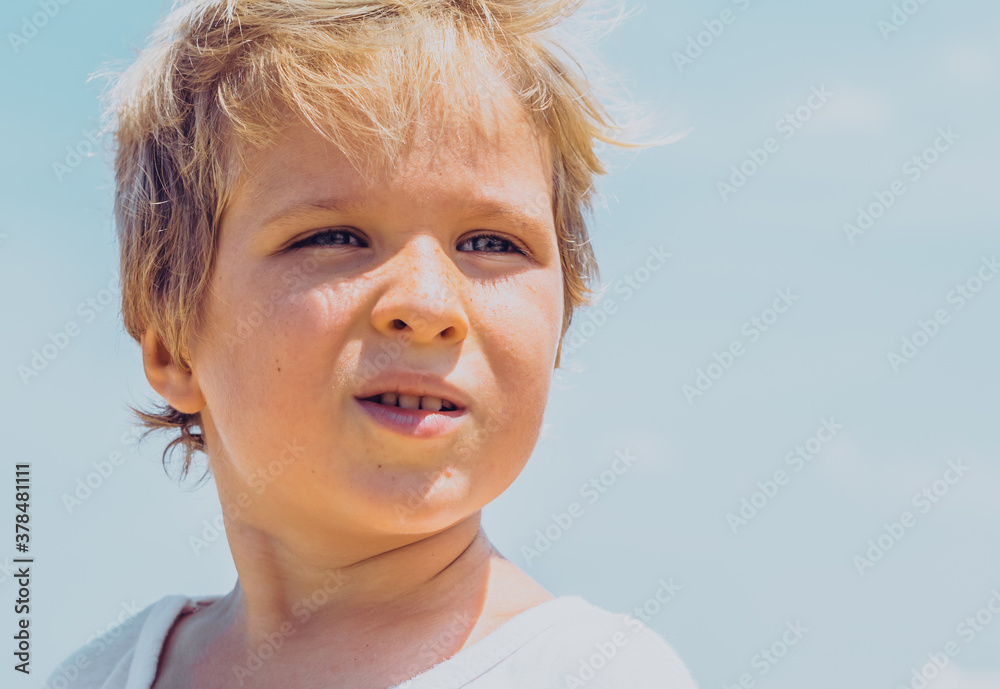 Close-up boy portrait . Serious male child squints a little in sunny weather looks into the distance. Clear blue sky background. 5 years old, freckles face, blue eyes, light t-shirt. Children concept Close-up boy portrait . Serious male child squints a little in sunny weather looks into the distance. Clear blue sky background. 5 years old, freckles face, blue eyes, light t-shirt. Children concept