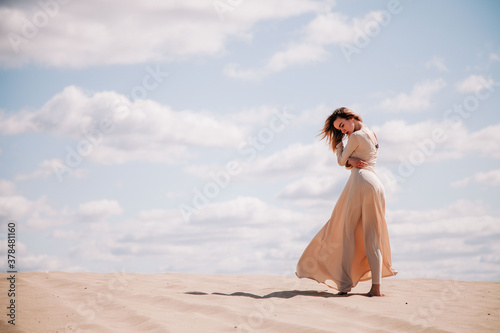 Young, slender girl in beige dress walks in the desert © Denis