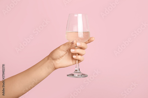 Hand with glass of wine on color background
