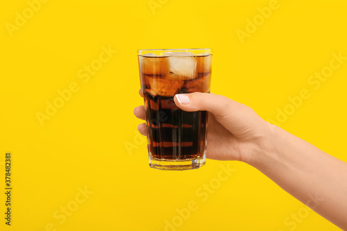 Hand with glass of tasty cola on color background