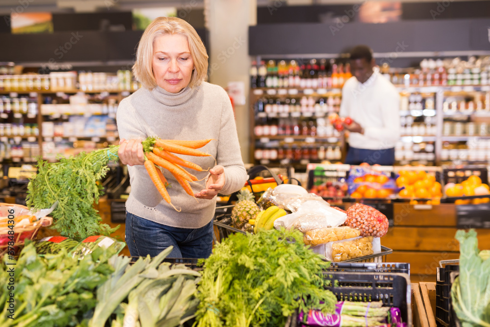 Pensive mature woman buying fresh organic vegetables in supermarket