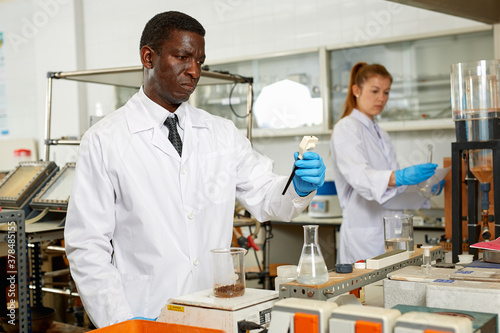 Focused man lab technician in gloves working with reagents and test tubes  woman on background