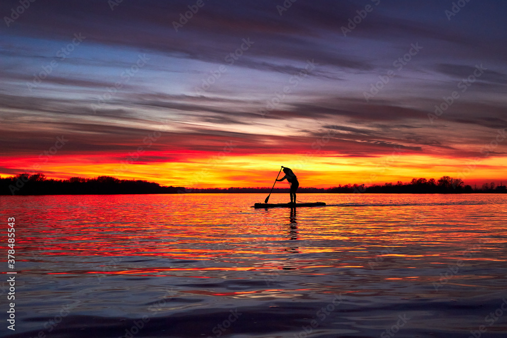 Silhouette of girl paddle on stand up paddle boarding (sup) on quiet river at winter sunset. Winter season and active leisure concept.