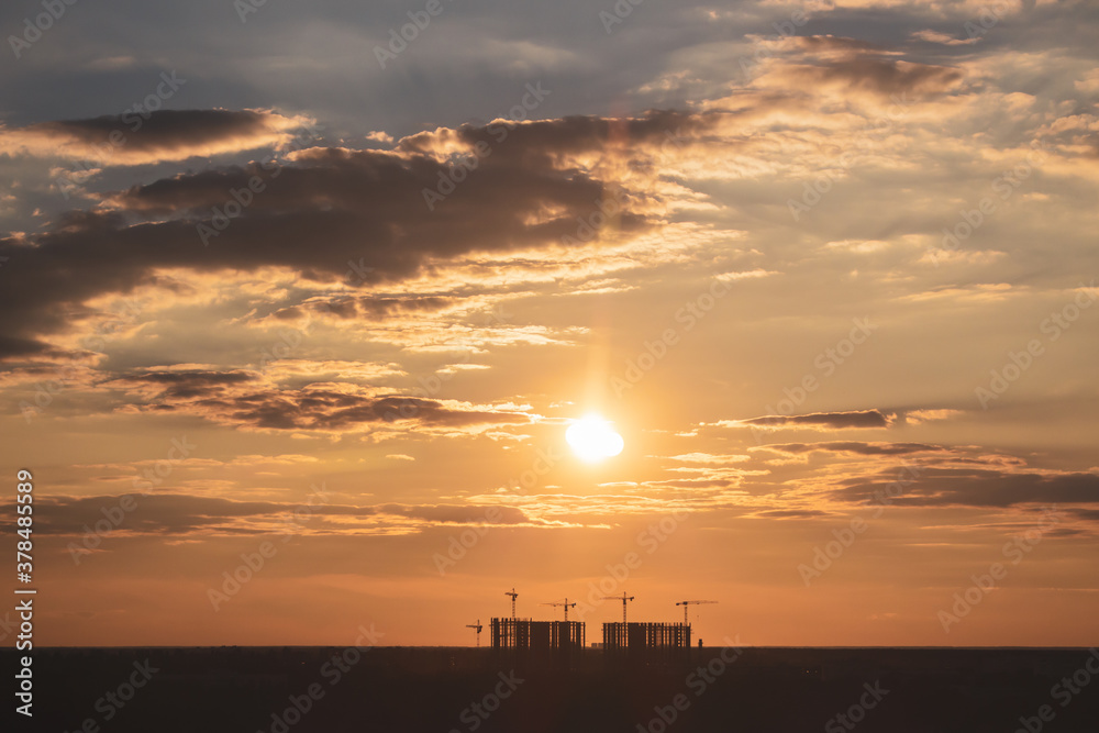 Tower cranes and buildings on horizon with evening sky, soft focus. Sunset over city. Construction with scenic evening sky and clouds above. Picturesque cityscape in evening haze. Buildings silhouette