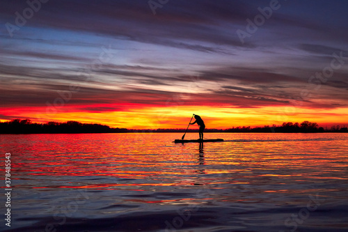 Silhouette of girl paddle on stand up paddle boarding (sup) on quiet river at winter sunset. Winter season and active leisure concept.