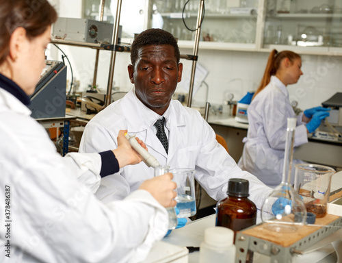 African american male lab technician writing report after chemical experiments with woman worker