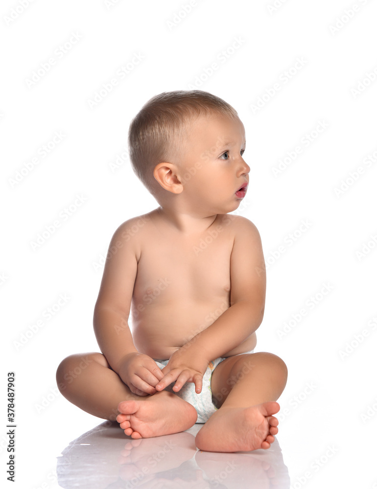 Baby boy toddler naked in diaper sits on the floor with head turned and looks aside Baby boy toddler naked in diaper sits on the floor with head turned and looks aside