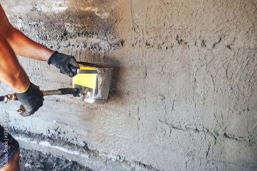 Man plastering a wall with mortar using a hopper bucket.