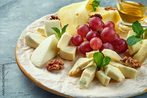 A plate of different cheeses served with grapes, nuts and honey. Appetizer Cheese Plate. Sliced Camembert, Brie, Parmesan blue cheese