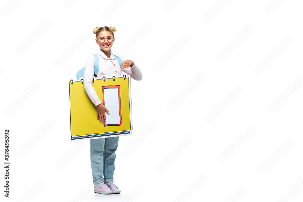 full length view of pleased schoolgirl in eyeglasses pointing with finger at paper cut copy book on white full length view of pleased schoolgirl in eyeglasses pointing with finger at paper cut copy book on white