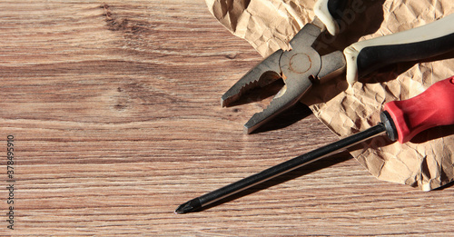 Screwdriver and pliers on a wooden background with crumpled paper. The tools are old. photo