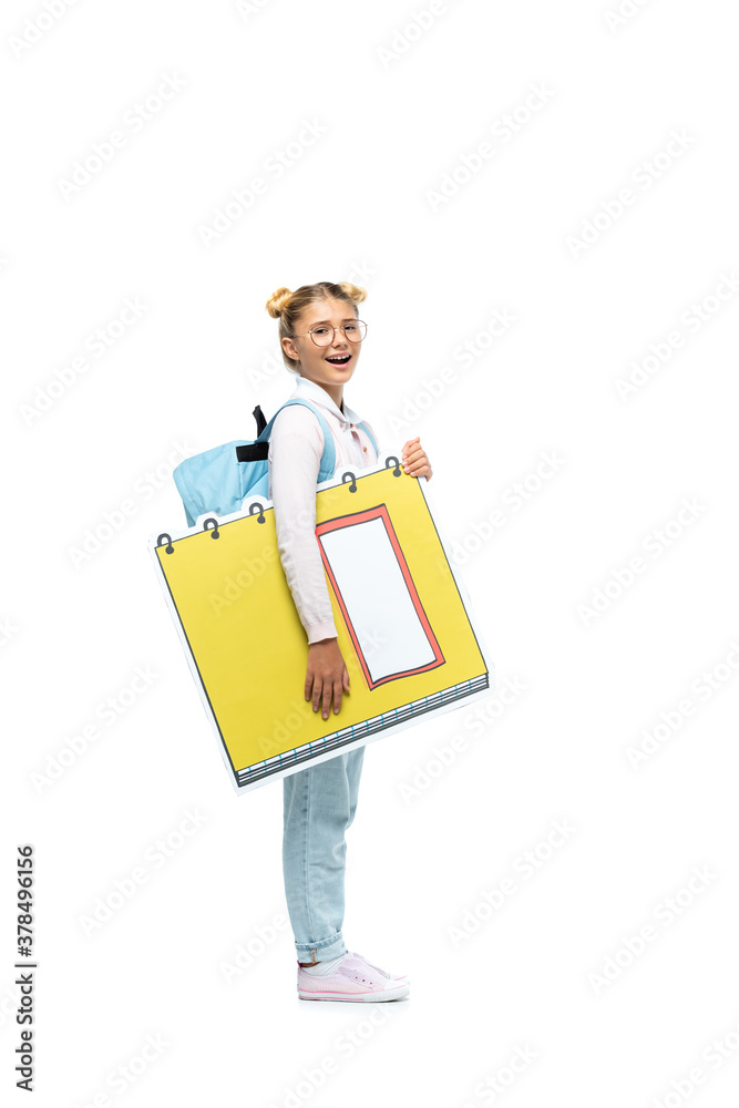 full length view of excited schoolgirl in eyeglasses holding paper cut copy book while looking at camera on white full length view of excited schoolgirl in eyeglasses holding paper cut copy book while looking at camera on white