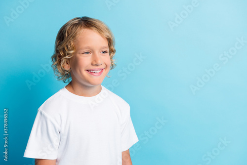 Photo of positive small boy look empty space toothy smiling wear white t-shirt isolated over blue color background