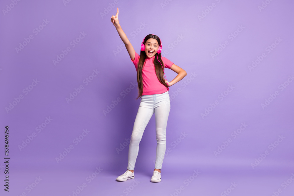 Full length body size photo of small girl smiling listening to music pointing with finger laughing isolated on purple color background Full length body size photo of small girl smiling listening to music pointing with finger laughing isolated on purple color background