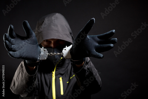 Thug or hucker in handcuffs and black clothes is arested. Concept: Crime because of crisis covid 19. isolated on black background photo