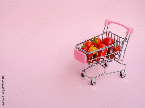 Pink shopping cart full of tomatoes on pink background