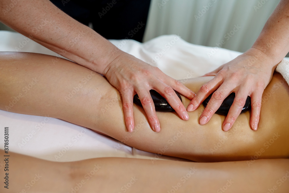 Massage therapist in a beauty salon giving a young woman a stone massage to relax the body and drain the lymph
