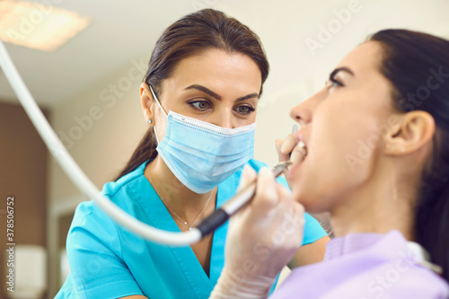 Serious dentist removing calculus from client's teeth with ultrasonic scaler in modern dental clinic