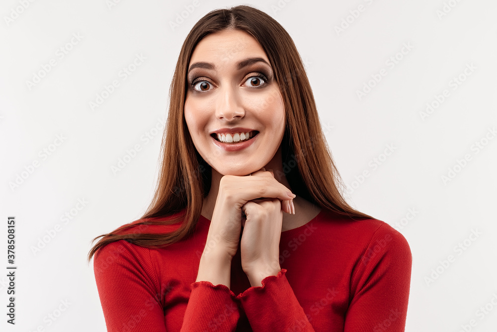Portrait of brunette dressed in casual red sweater keeping hands together near chin. Studio shot, white background Portrait of brunette dressed in casual red sweater keeping hands together near chin. Studio shot, white background