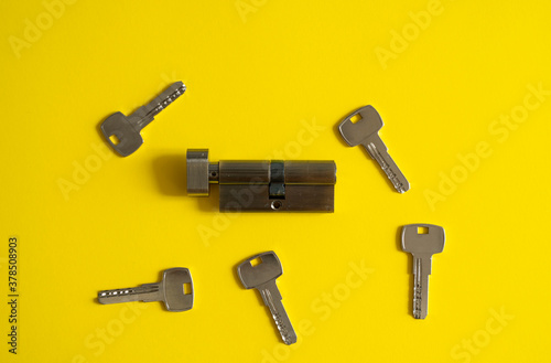A door lock cylinder core with keys on the yellow background. The cylinder of the lock with keys. Installing a new lock on the door. Spare parts for the door.