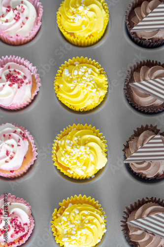 Variety of cupcakes in a metal baking tray. Grey wood background