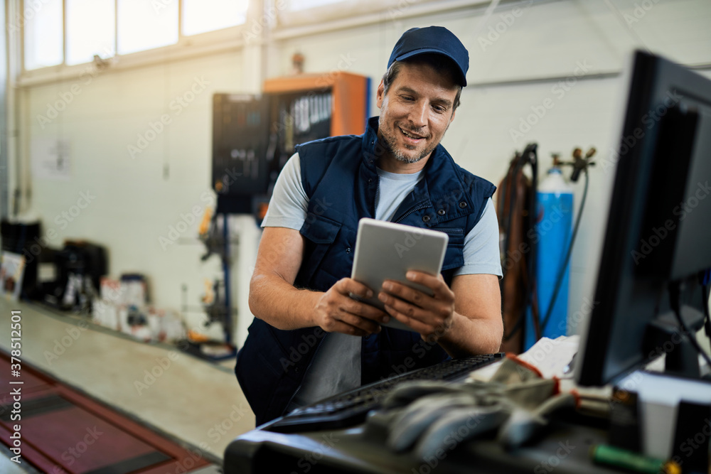 Happy auto repairman working on touchpad in a workshop. Happy auto repairman working on touchpad in a workshop.