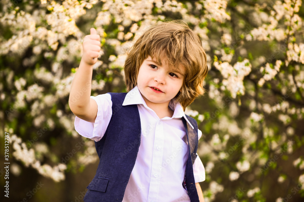 small boy at blossoming spring tree. happy kid has lush healthy hair. summer and spring fashion. child enjoy blooming nature in part. childhood happiness. carefree boy show thumb up small boy at blossoming spring tree. happy kid has lush healthy hair. summer and spring fashion. child enjoy blooming nature in part. childhood happiness. carefree boy show thumb up