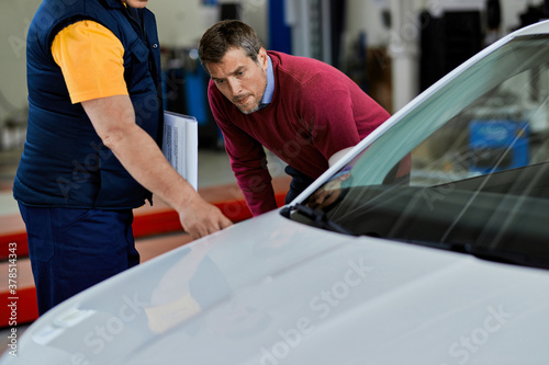Male customer and mechanic examining car in auto repair shop.