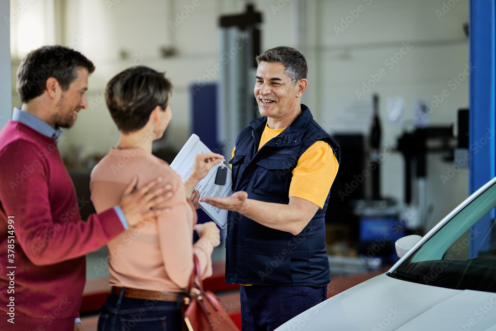 Obraz premium Happy auto repairman receiving car key from his customers in a workshop.