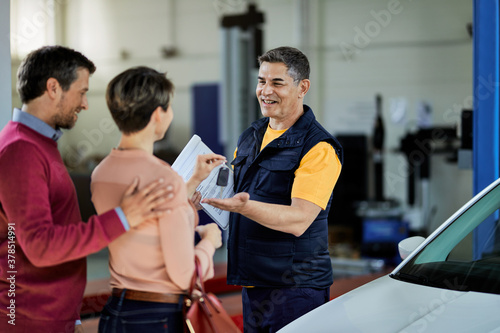 Happy auto repairman receiving car key from his customers in a workshop.