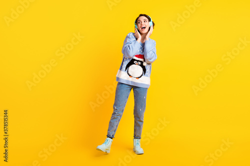 Full body photo of attractive funny lady student x-mas party newyear listen cool modern technology earphones wear ugly ornament sweater pullover jeans shoes isolated yellow color background