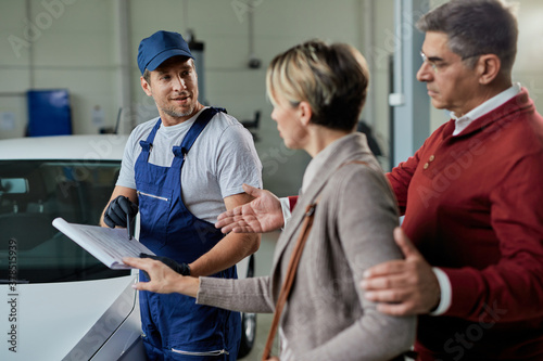 Happy mechanic and his customers going through check list in auto repair shop.