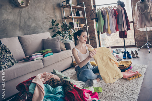 Full body focused girl house wife prepare for garage sale auction look pack her used dressing clothes pile stack sit floor carpet legs crossed folded in house indoors photo