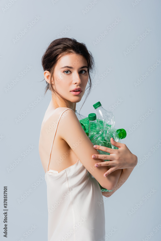 brunette woman in silk dress holding empty and plastic bottles isolated on grey, ecology concept brunette woman in silk dress holding empty and plastic bottles isolated on grey, ecology concept