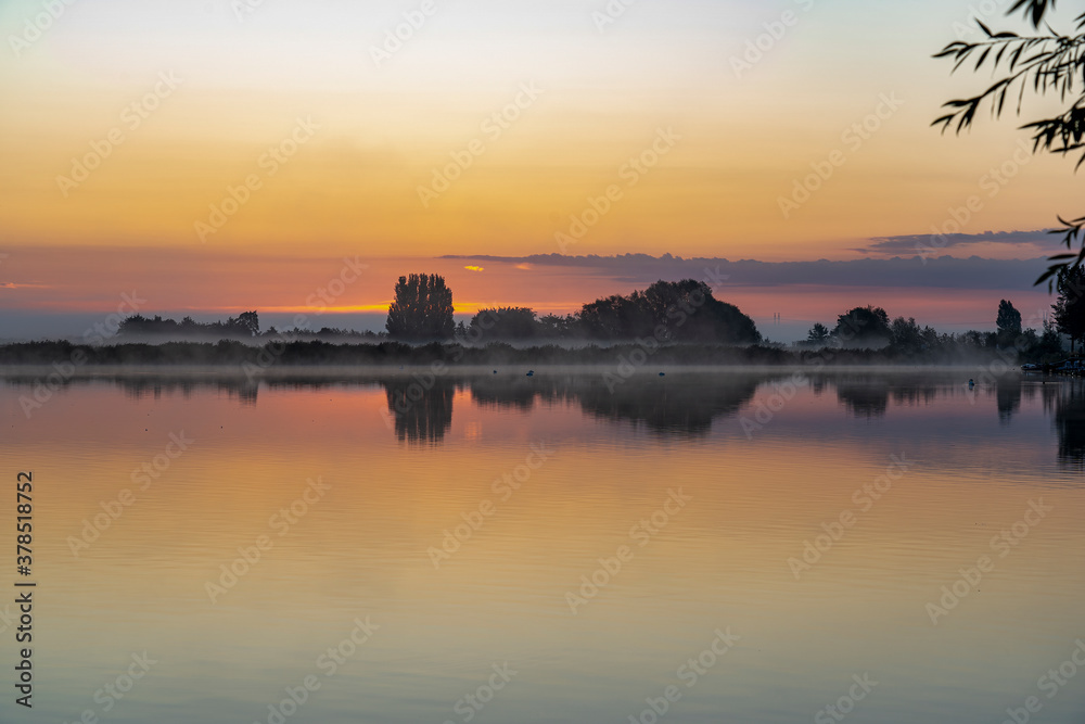 Just before sunrise, the morning mist above lake Noordhovense plas and the clouds above the horizon, create a colorful spectacle