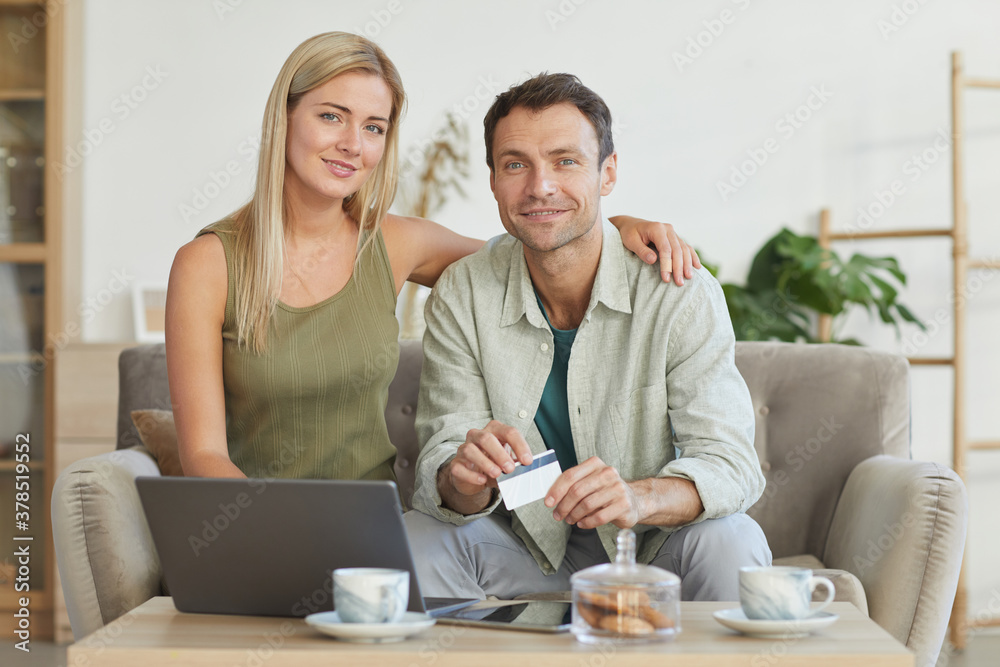 Portrait of young couple smiling at camera while paying for purchases online with credit card using laptop computer Portrait of young couple smiling at camera while paying for purchases online with credit card using laptop computer